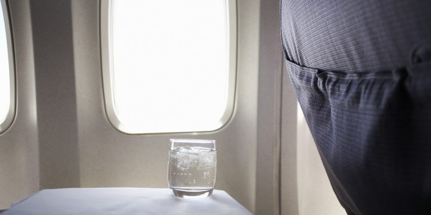 Glass of water on airplane tray table by window